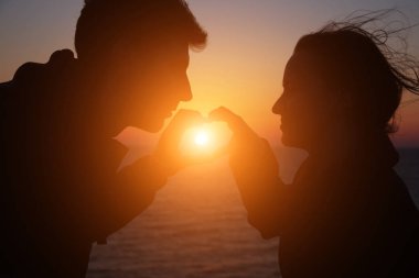 Siluet adam ve kız güzel bir gün batımında el ele tutuşuyorlar.