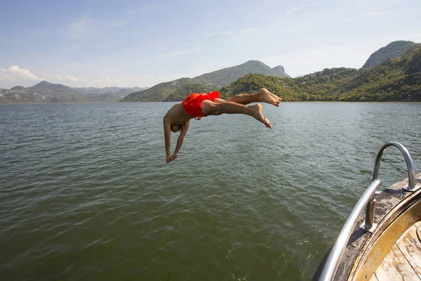 暑い夏の日に船の向こうの少年 ヨットから海の青の中に爽やかなお風呂の男 衣装を着た少年が海に飛び込み — ストック写真