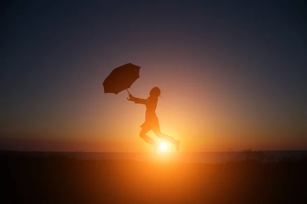 Silhouet Van Een Meisje Met Een Paraplu Bij Zonsondergang Springen — Stockfoto
