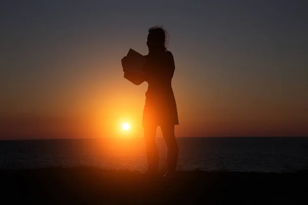 自分たちの手で本と美しい夕日の背景に女の子のシルエット — ストック写真