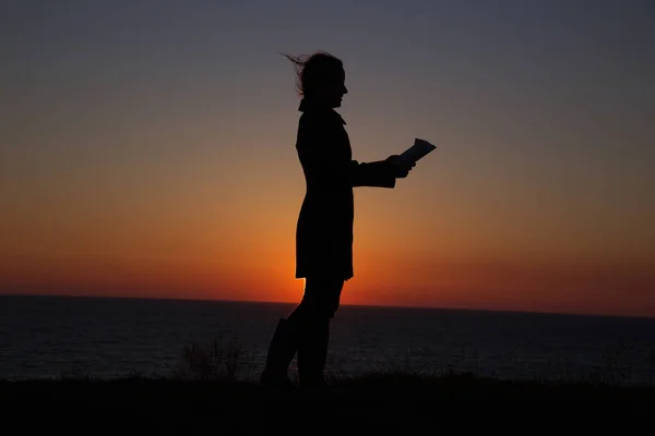 silhouette of a girl reading an interesting book on the background of a beautiful sunset