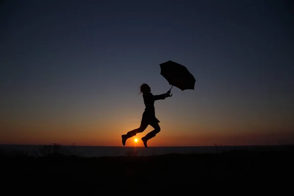 Silhouet Van Een Meisje Met Een Paraplu Bij Zonsondergang Springen — Stockfoto