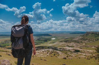 Sırt çantalı bir yürüyüşçü dağın tepesinde dinleniyor ve vadi manzarasının tadını çıkarıyor.