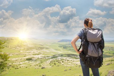 Sırt çantalı bir yürüyüşçü dağın tepesinde dinleniyor ve vadi manzarasının tadını çıkarıyor.