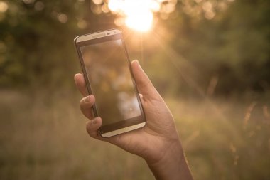 Elini tut siyah akıllı telefon, cep telefonu, mobil yeşil orman arka plan bulanık görüntü üzerinde