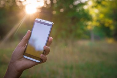 Elini tut siyah akıllı telefon, cep telefonu, mobil yeşil orman arka plan bulanık görüntü üzerinde