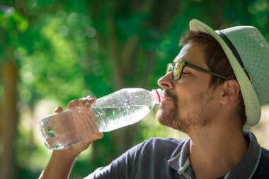 Kameraya bakarak ormandaki oturan gülümseyen adam. su adam. ağaç ve sırt çantası