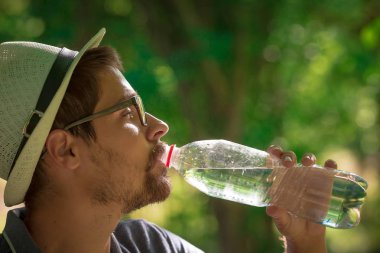 Kameraya bakarak ormandaki oturan gülümseyen adam. su adam. ağaç ve sırt çantası