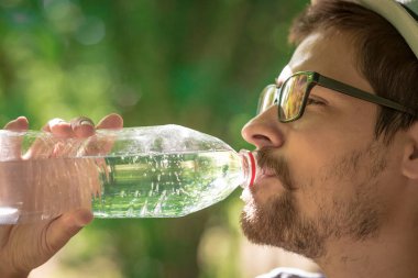 Kameraya bakarak ormandaki oturan gülümseyen adam. su adam. ağaç ve sırt çantası