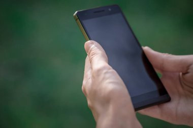 Elini tut siyah akıllı telefon, cep telefonu, mobil yeşil orman arka plan bulanık görüntü üzerinde