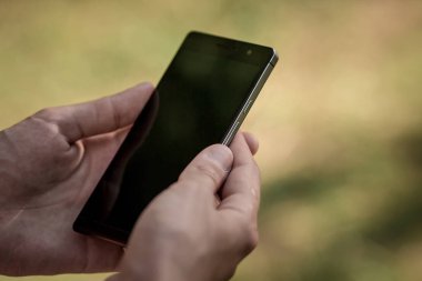 Elini tut siyah akıllı telefon, cep telefonu, mobil yeşil orman arka plan bulanık görüntü üzerinde