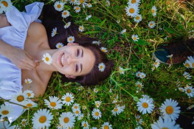 Güzel bir kadın papatya tarlasından zevk alıyor, güzel bir kadın çiçek bahçesinde uzanıyor, güzel bir kız dışarıda dinleniyor, eğleniyor, çiçek tutuyor, mutlu genç bayan ve bahar yeşili doğa, uyum kavramı.