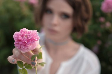 Bahçede güllerin yanında poz veren kıvırcık saçlı güzel bir genç kadın. Parfüm reklamı konsepti.