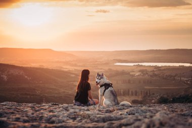 Gün batımında dağlarda bir köpek (gri ve beyaz husky) ile güzel kız çalış