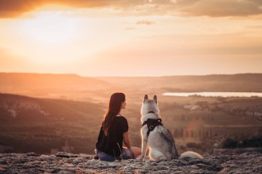 Gün batımında dağlarda bir köpek (gri ve beyaz husky) ile güzel kız çalış