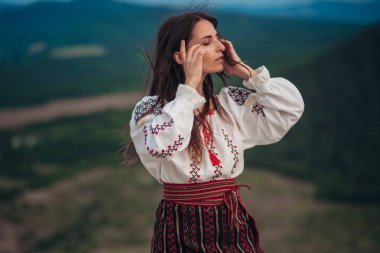 Atractive kadın geleneksel Romen kostüm dağda yeşil arka plan bulanık. Açık fotoğraf. Gelenekler ve kültürel çeşitlilik