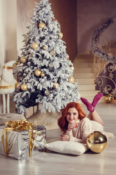 Noel ağacı yakınındaki şömine tarafından curlu saç hediyelerle mutlu genç bayan. Yeni yıl kavramı.