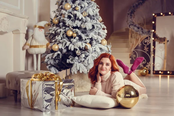 Noel ağacı yakınındaki şömine tarafından curlu saç hediyelerle mutlu genç bayan. Yeni yıl kavramı.