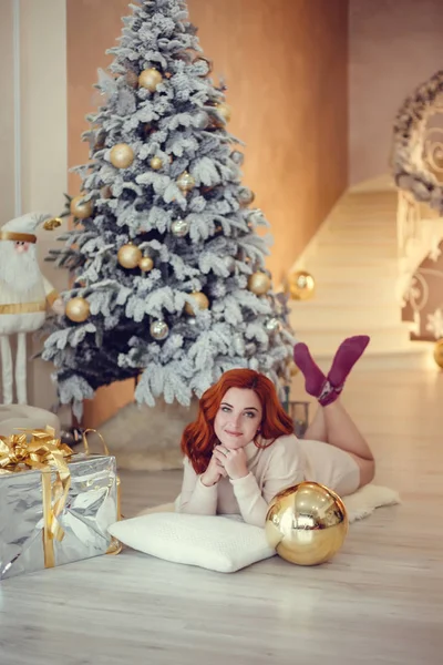 Noel ağacı yakınındaki şömine tarafından curlu saç hediyelerle mutlu genç bayan. Yeni yıl kavramı.