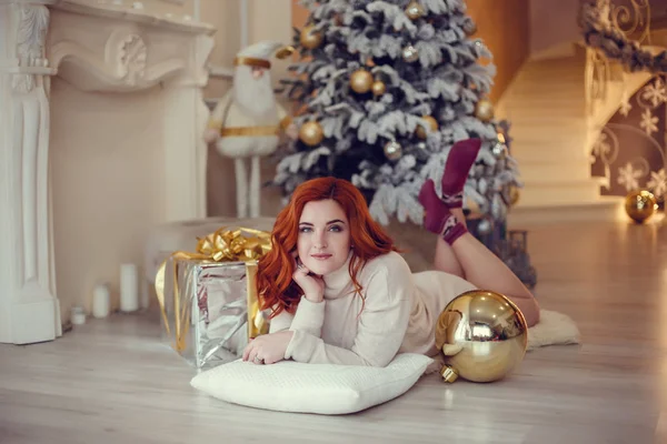 Noel ağacı yakınındaki şömine tarafından curlu saç hediyelerle mutlu genç bayan. Yeni yıl kavramı.