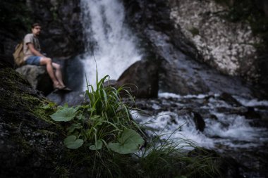 Genç yalınayak turist giyen kot pantolon kısa ve büyük kayanın üzerinde oturan sırt çantası