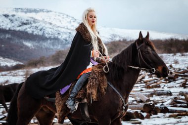 Güzel genç sarışın bir karga üzerinde. Dağlar arka planı siyah bir at ile kadın viking