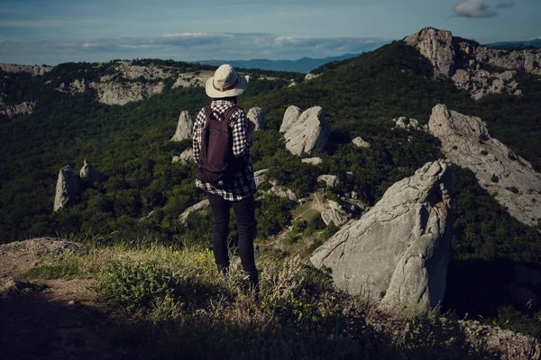 Femeie călător cu rucsac care deține pălărie și se uită la munți și pădure uimitoare, conceptul de călătorie rătăcire, spațiu pentru text, moment epic atmosferic — Fotografie, imagine de stoc