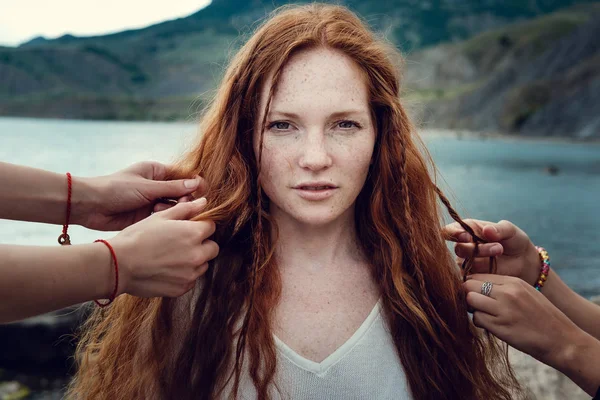 Red-haired girl with hippies with freckles, whose hair is braided by two friends — Stock Photo, Image