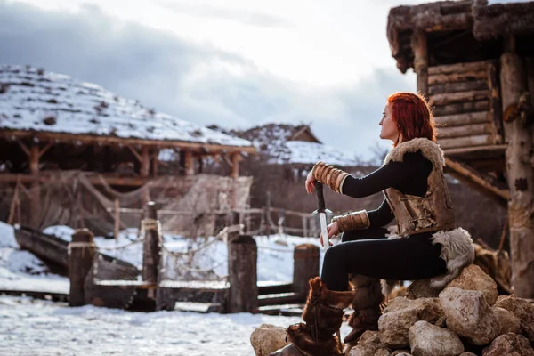 Rudowłosa kobieta jest Viking. Na tle wieś lub osady. W rękach miecz — Zdjęcie stockowe
