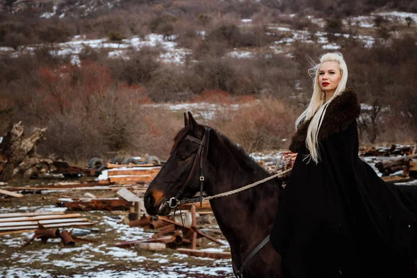 Güzel genç sarışın bir karga üzerinde. Dağlar arka planı siyah bir at ile kadın viking — Stok fotoğraf