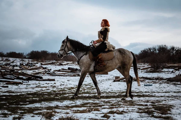 Menina bonita no cavalo e com cabelo vermelho na armadura. A mulher é uma Viking. Fantasia — Fotografia de Stock