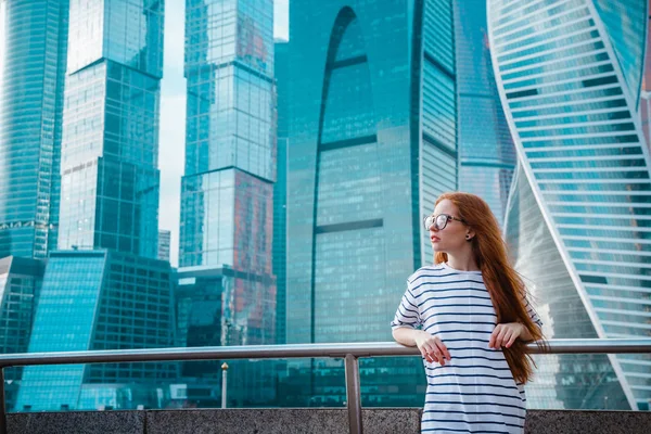 Belle femme souriante en manteau léger sur fond de gratte-ciel centre d'affaires d'une grande ville — Photo