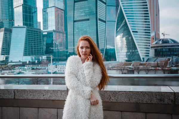 Sorrindo mulher bonita em um casaco leve contra o pano de fundo de um arranha-céus centro de negócios de uma cidade grande — Fotografia de Stock