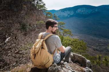 Genç hipster adam bahar dağlarda. Hipster arkasından bir sırt çantası ile bir gezi gider,