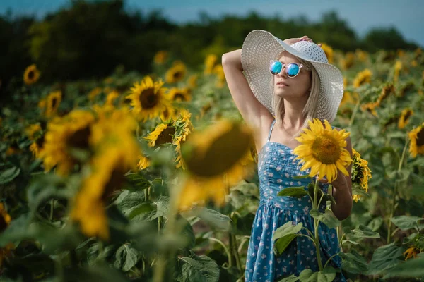 Belle fille sexy douce dans une robe bleue marchant sur un champ de tournesols, souriant un beau sourire, fille gaie, style de vie, idéal pour la publicité et la photo soleil brille lumineux et juteux — Photo