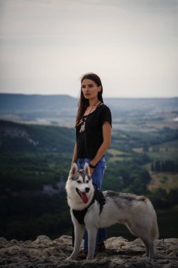 Güzel kız bir köpeği, gri ve beyaz husky, gün batımında dağlarda çalış.