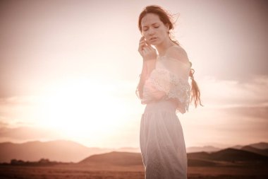 Kızıl saçlı kız beyaz elbise gülümser buğday dolu bir alanda hoş bir gülümsemeniz