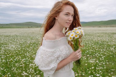 Papatya alanındaki kıvırcık kırmızı saçlı güzel genç kız