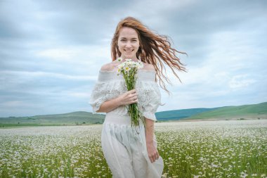 Papatya alanındaki kıvırcık kırmızı saçlı güzel genç kız