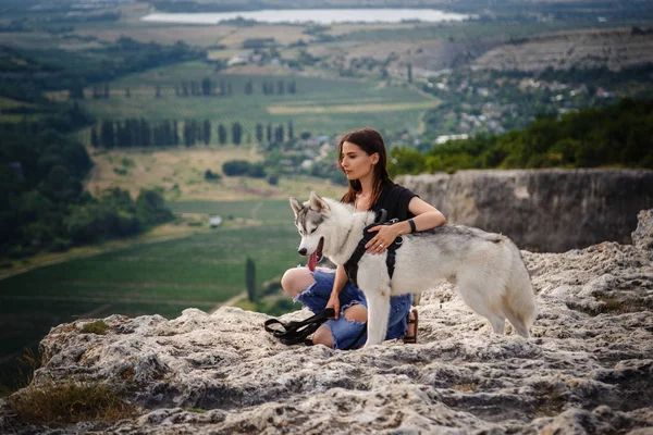 Vacker flicka leker med en hund, grått och vitt husky, i bergen i solnedgången. — Stockfoto