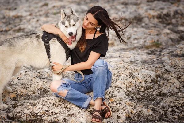 Vacker flicka leker med en hund, grått och vitt husky, i bergen i solnedgången. — Stockfoto