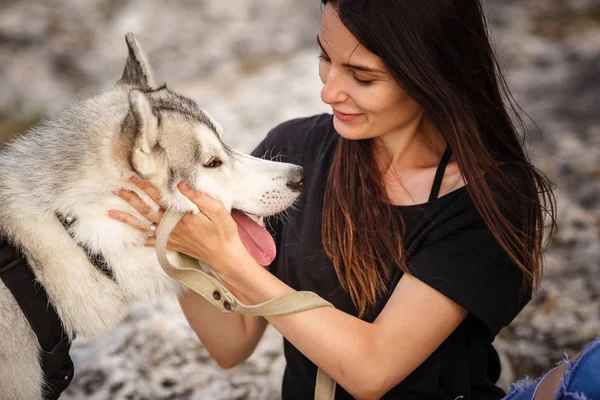 Bella ragazza gioca con un cane, grigio e bianco husky, in montagna al tramonto . — Foto Stock