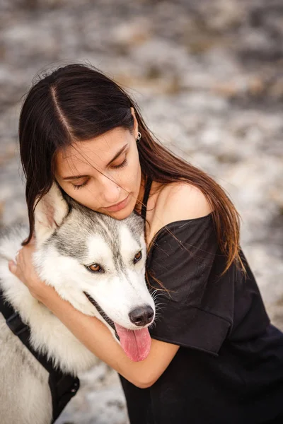 Bella ragazza gioca con un cane, grigio e bianco husky, in montagna al tramonto . — Foto Stock