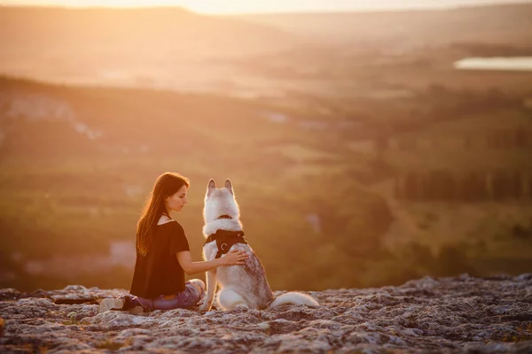 Bella ragazza gioca con un cane, grigio e bianco husky, in montagna al tramonto — Foto Stock