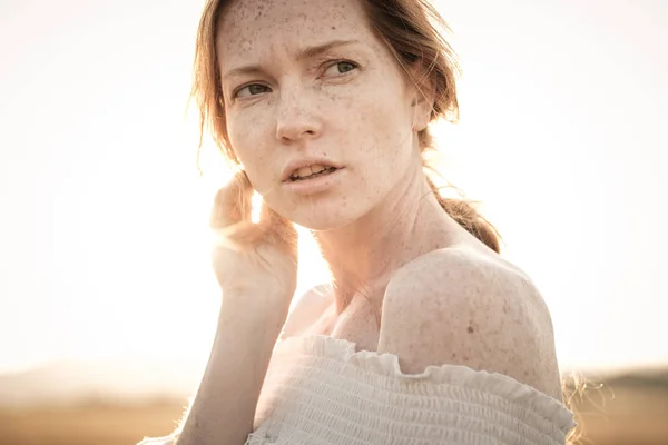 Menina ruiva em um campo de trigo em um vestido branco sorri um lindo sorriso — Fotografia de Stock