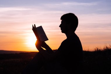 Parkta gün batımına karşı kitap okuyan adam..