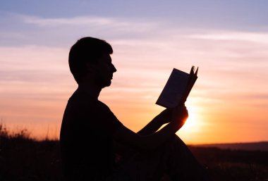 Parkta gün batımına karşı kitap okuyan adam..