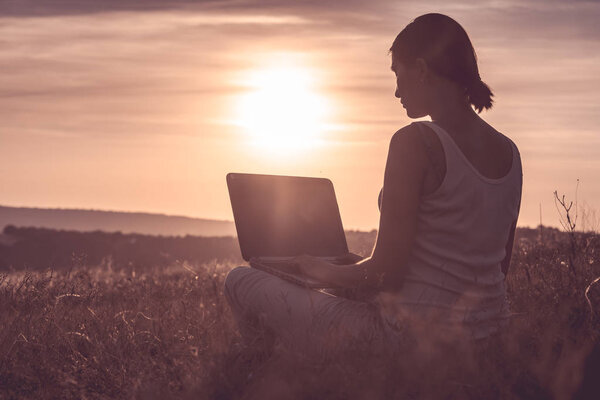 Silhouette of a girl with laptop on sunset or sunrise background. Freedom at work