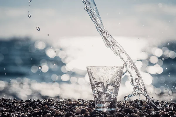 Splashing water in a glass by the sea — Stock Photo, Image