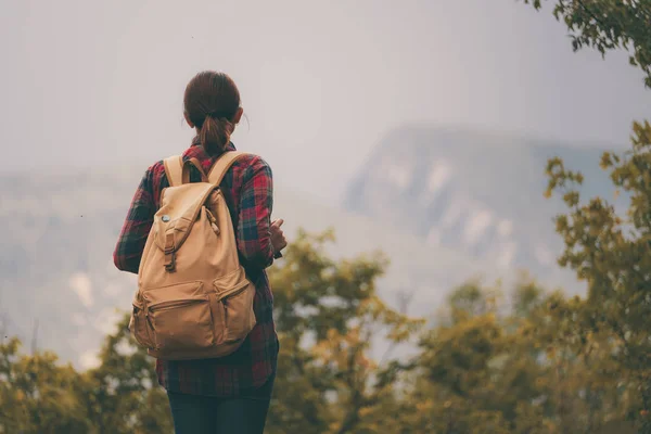 Hipster young girl with backpack enjoying sunset on peak of foggy mountain. — Stock Photo, Image